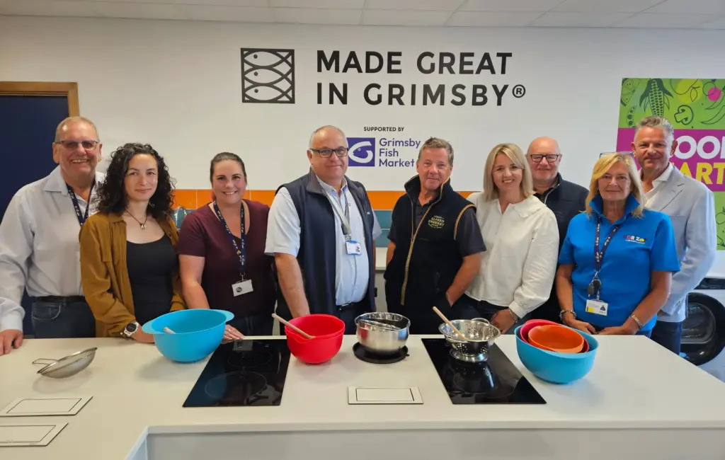 Stakeholders in Horizon Youth Zone's training kitchen with the Made Great in Grimsby and Grimsby Fish Market branding displayed.
